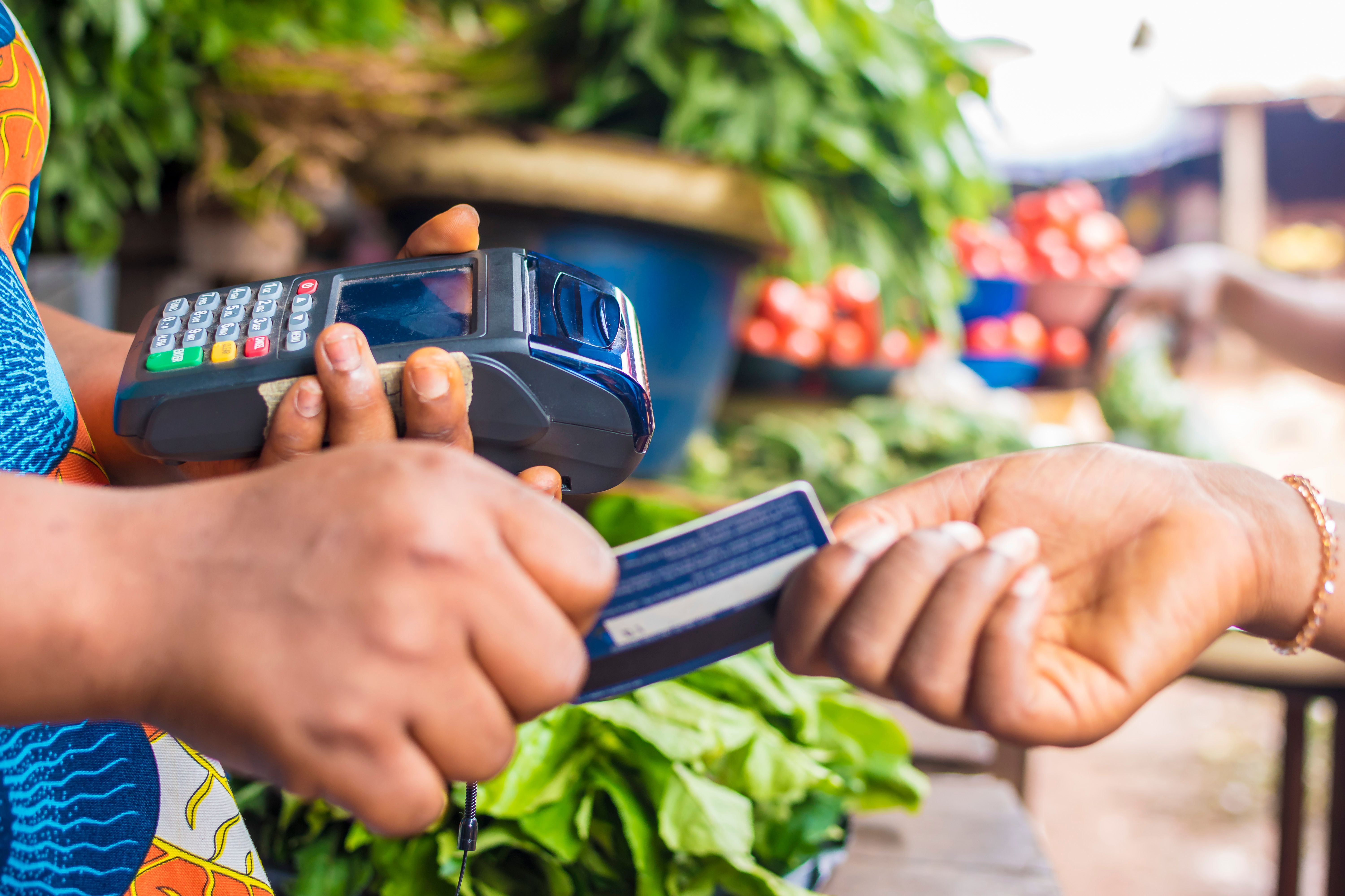 black woman holding a pos system collecting a credit card from someone in a market