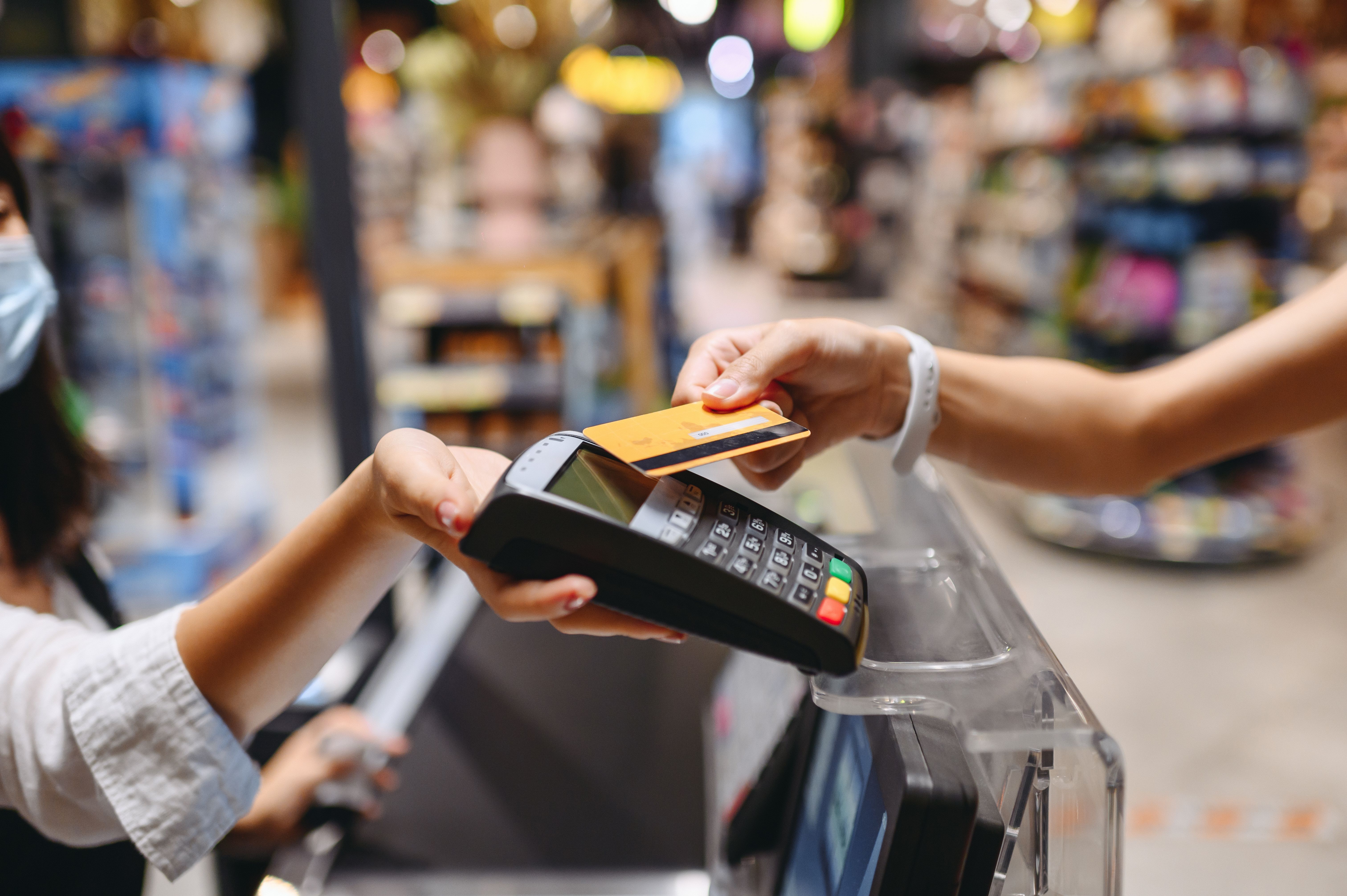 Cropped close up woman hand arm shopping at supermarket put credit card to wireless modern bank payment terminal process acquire payments near cashier checkout inside store. People purchasing concept
