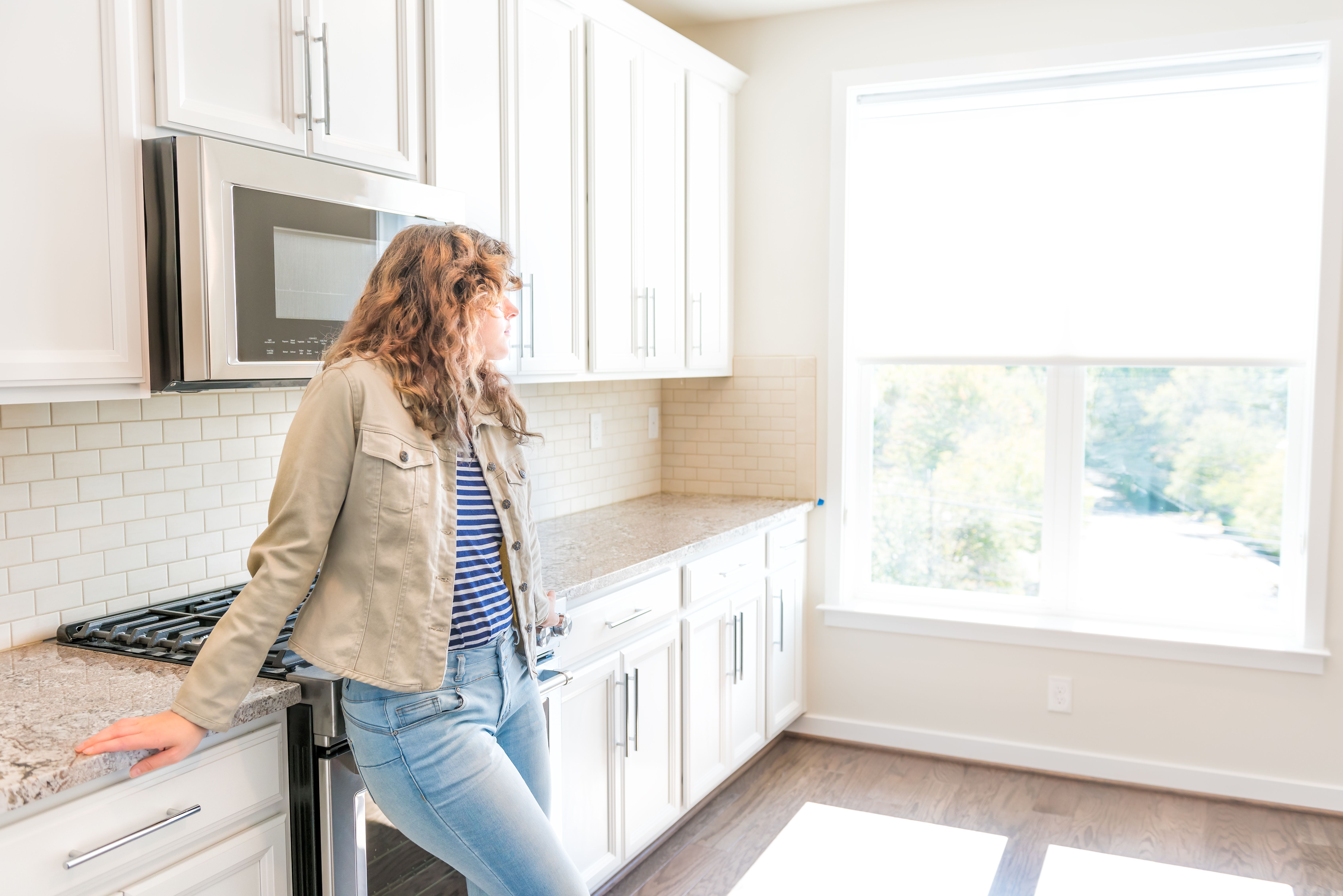 One young woman standing in kitchen in clean, modern, white home design before move-in