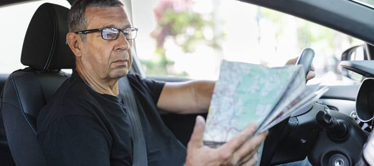 Older man behind the steering wheel looking at map for directions.