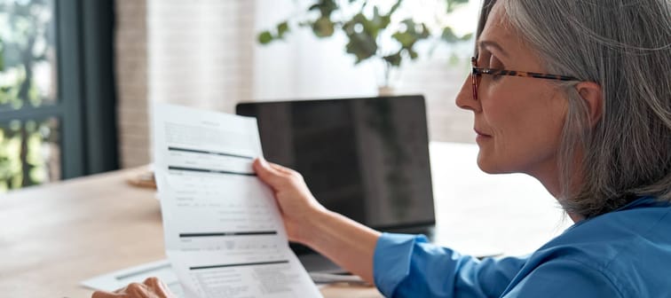 Mature woman reviewing expenses and using a calculator to cut costs