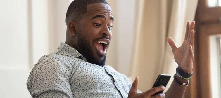 Excited black man sitting on a couch looking at his phone reacting to BoC rate drop