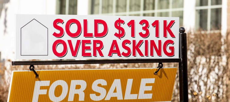 A real estate For Sales sign with  a Sold $131K Over Asking notice suggesting a hot or overheated housing market