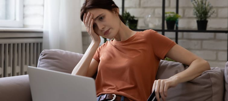 Woman stressed on her laptop while holding credit card