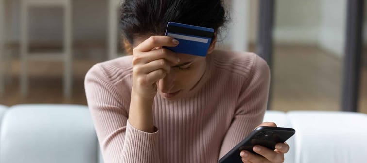 Upset female with head and credit card in one hand and phone in the other sitting on couch