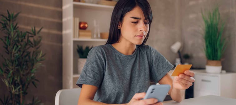 Side view shot of a beautiful businesswoman looking down curiously to her credit card information while holding her cell phone in the other hand.