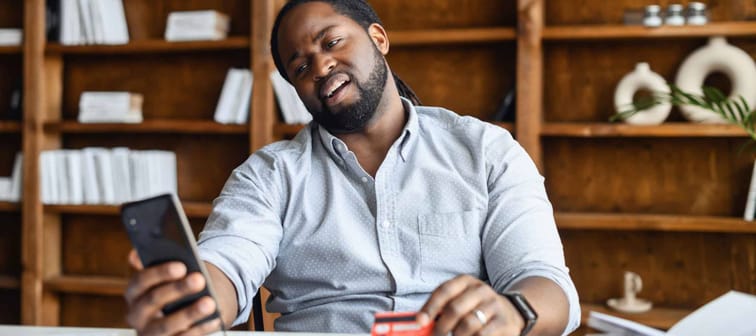 man looking disappointed at his phone while holding a credit card