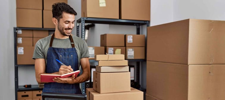 Young hispanic man business worker writing on notebook at storehouse