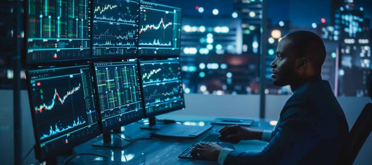 Financial Analyst Working on Computer with Multi-Monitor Workstation with Real-Time Stocks,  Late at Night.