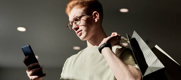 Gen Z male looking at phone while carrying shopping bags