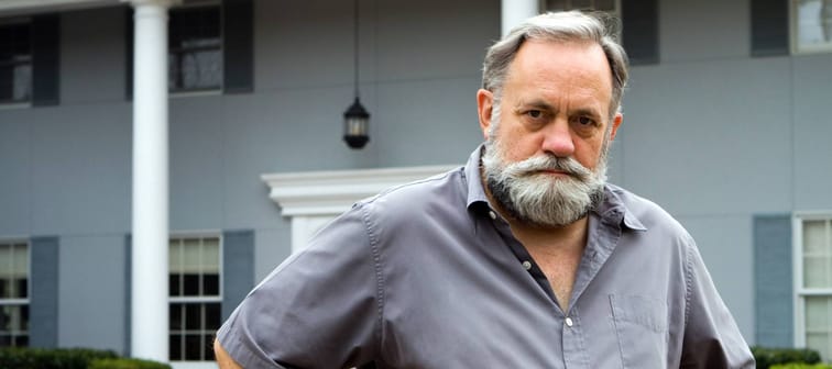 Unhappy older man stands in front of his home.