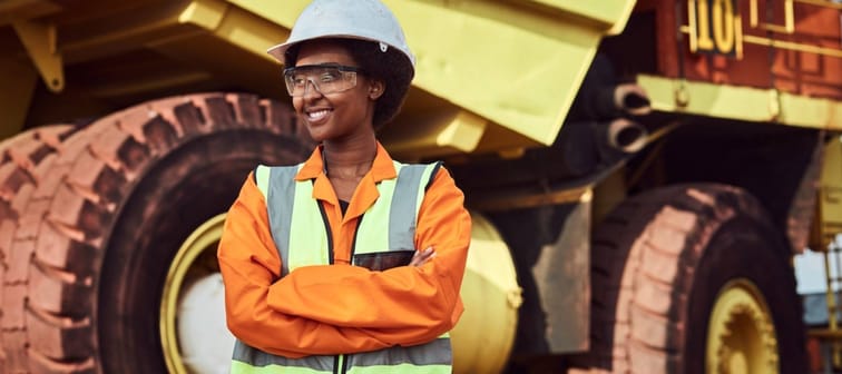 A young female miner standing in front of a large haul dump truck wearing her personal protective wear