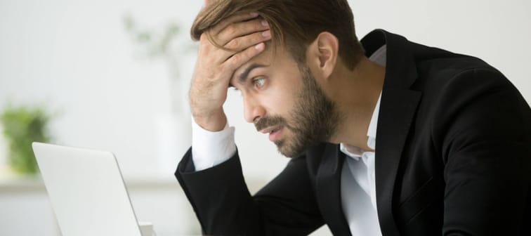 Worried stressed businessman in suit shocked by bad news using laptop at work