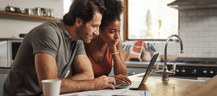 Young couple filling out information on laptop, sitting in kitchen