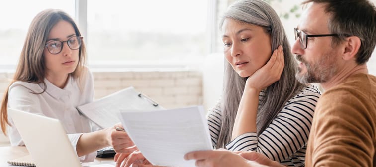 Middle age couple sitting in front of laptop and papers discussing finances with advisor