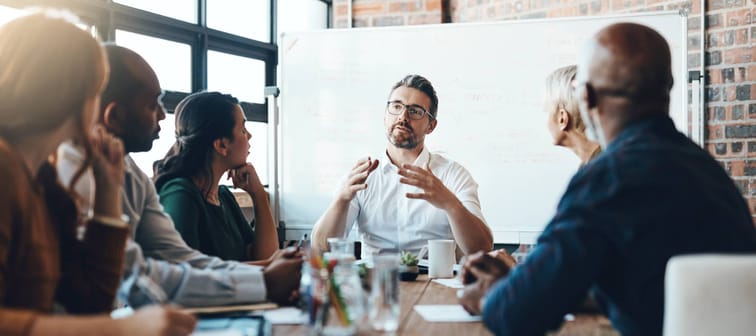 Manager leading meeting at boardroom table surrounded by employees