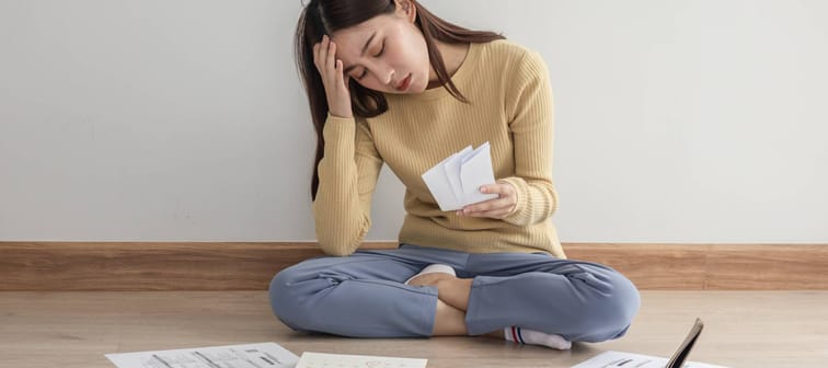 Stressed young woman sitting on floor surrounded by bills