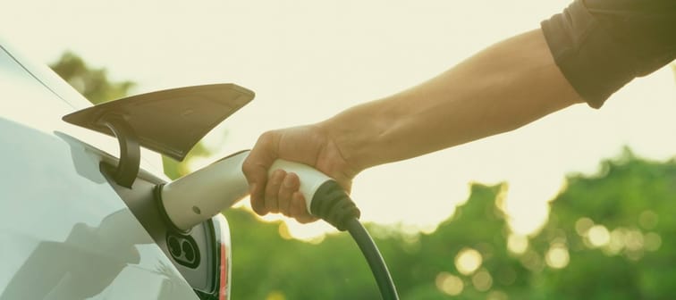 Man recharging battery for electric car during autumnal road trip