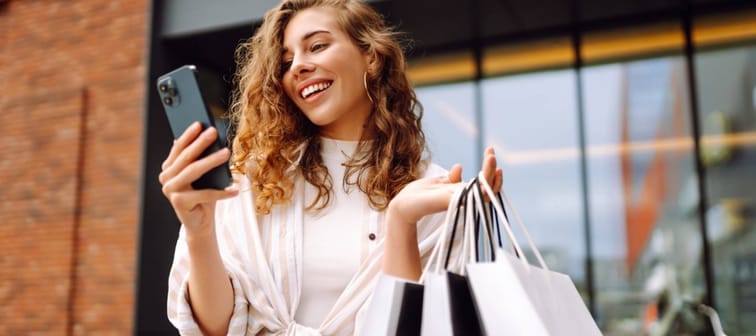 Young woman holding shopping bags and looking at her phone