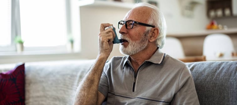 Mature man using medical inhaler to prevent and treat wheezing and shortness of breath