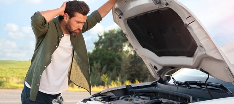 Upset man looking under hood of broken car outdoors