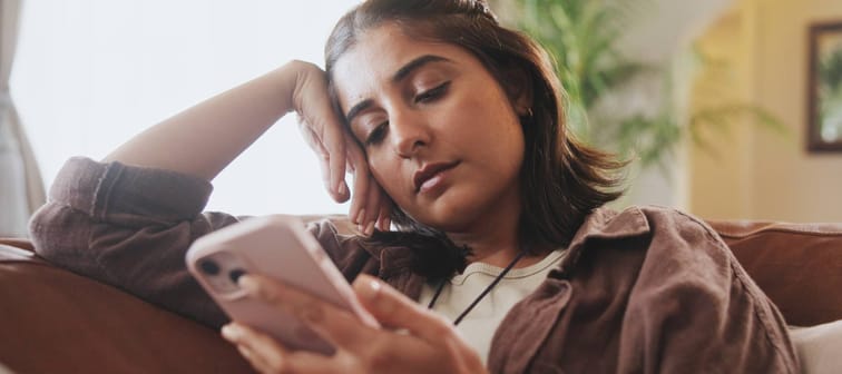 Young woman scrolling through phone on couch