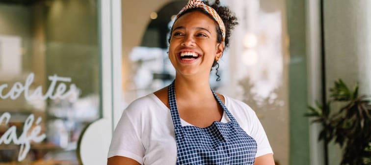 Happy young entrepreneur embraces technology in a vibrant café, holding a digital tablet in hand.