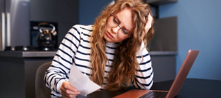 Unhappy woman calculates expenses on bills, upset about increased utilities prices.