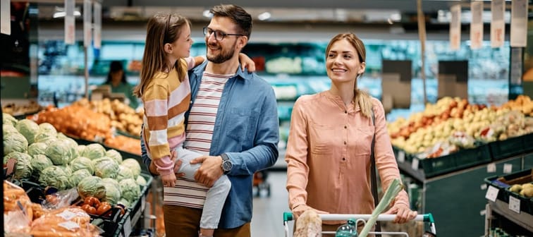 Happy parents with small daughter shopping in supermarket