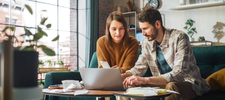 Couple Using Laptop Computer, Sitting on Sofa in Apartment.