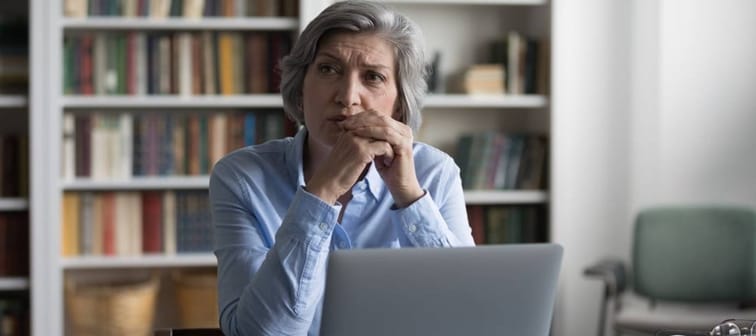 A woman looks away from her laptop pensively.