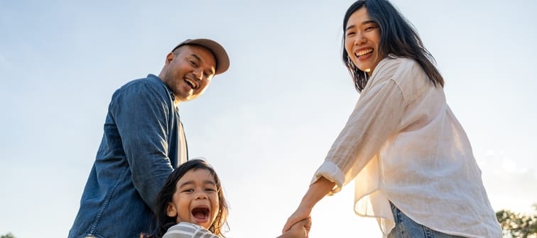 A family of 3 outside looking down at the camera and smiling.