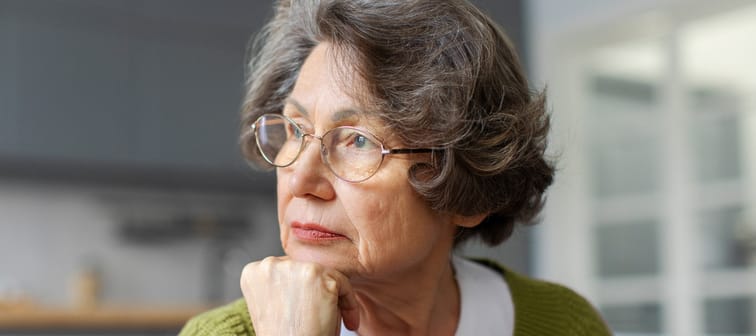 Pensive senior woman resting on sofa at home looking out window.