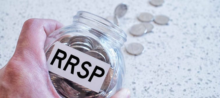 Hand holding glass jar with many coins and RRSP word over a marble counter top.Canadian Registered Retirement Savings fund concept.
