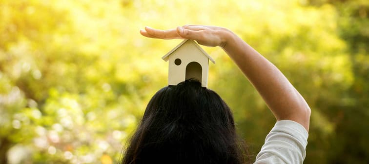 A women hand holding house model on head in the public park, Buying a new home for family concept.