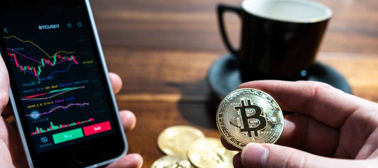 Smartphone with Bitcoin trading chart on the screen. Holding in hand a gold Bitcoin Cash coin. Trading on the cryptocurrency exchange.