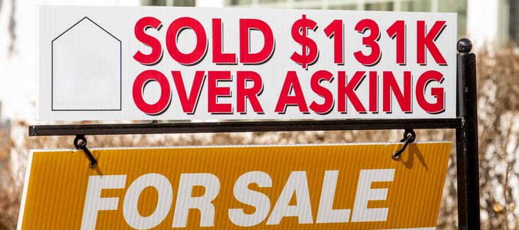 A real estate For Sales sign with  a Sold $131K Over Asking notice suggesting a hot or overheated housing market