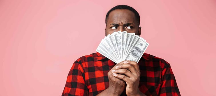 Portrait of a confused african man wearing shirt standing isolated, showing money banknotes