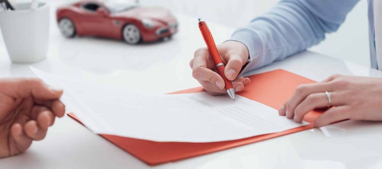 Woman signing auto insurance policy, while man holds the sheet