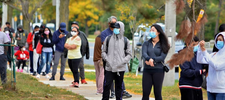 People wearing masks wait in line on the sidewalk for COVID tests