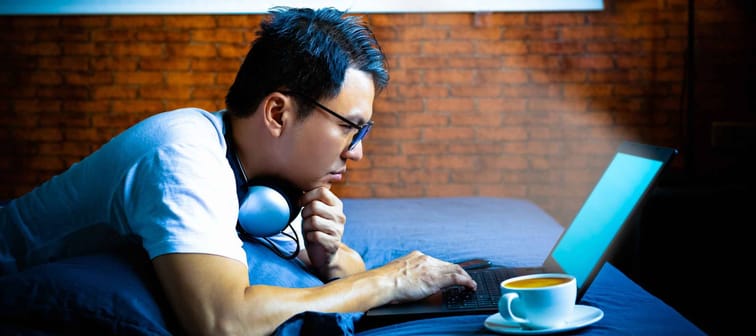 young asian man staring at laptop computer screen in bedroom at night. eye problems concept