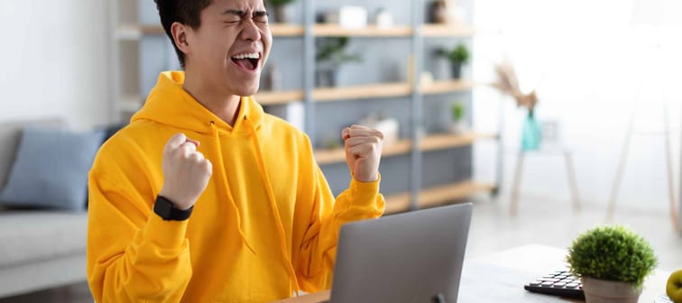 happy man joyful by laptop fists clenched celebrating