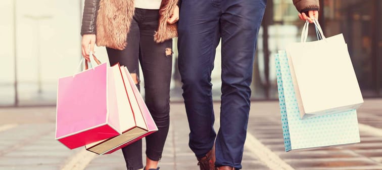 mid shot of couple holding hands and shopping bags walking