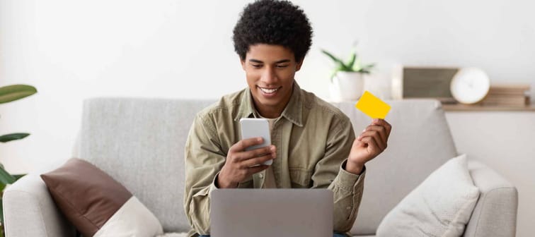 black male holding credit card slightly smiling sitting on couch behind laptop