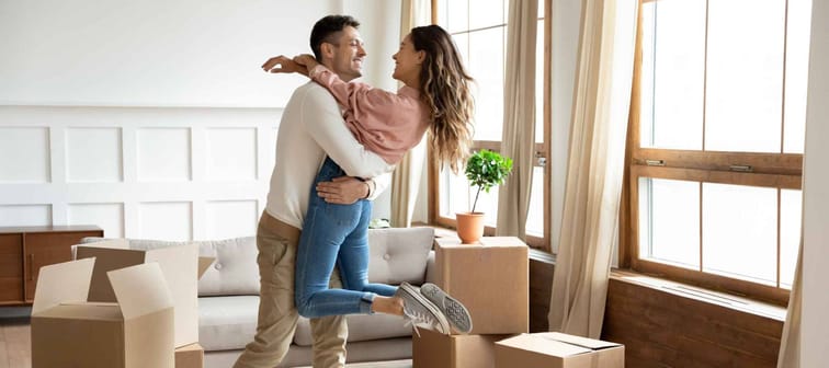 Happy young husband lifting excited wife celebrating moving day