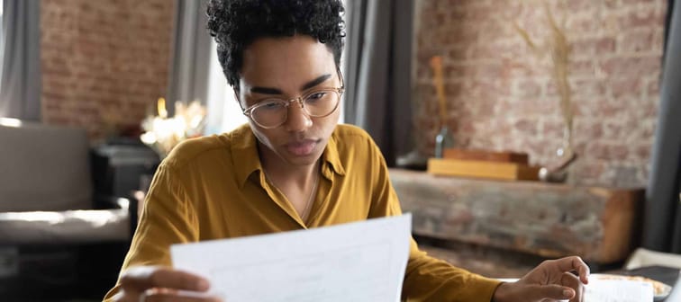 Focused young African American woman in eyeglasses looking through paper documents, managing business affairs, summarizing taxes, planning future investments, accounting alone at home office.