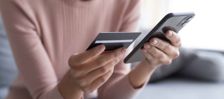 Close up female hands holding credit card and smartphone, young woman paying online, using banking service, entering information, shopping, ordering in internet store, doing secure payment