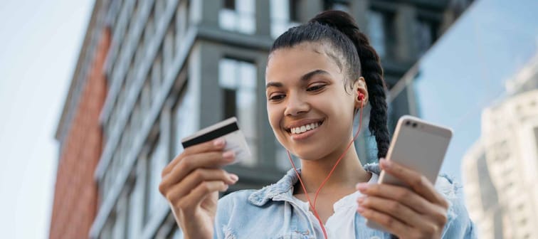 African American woman holding credit card, using smartphone.