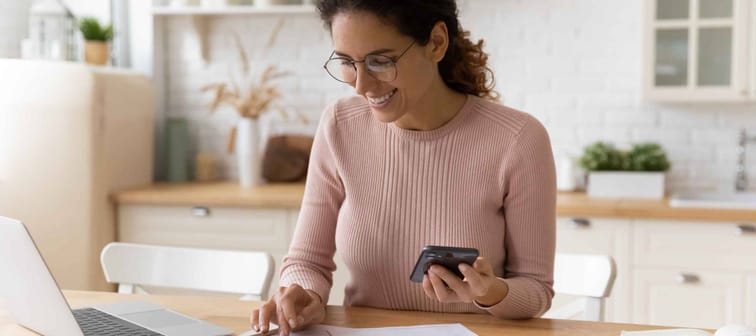 Young latina female work with financial papers at home count on calculator before paying taxes receipts online by phone.