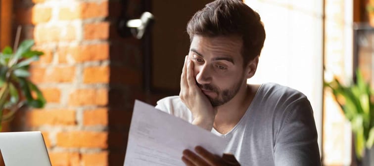 Confused frustrated young man reading letter in cafe